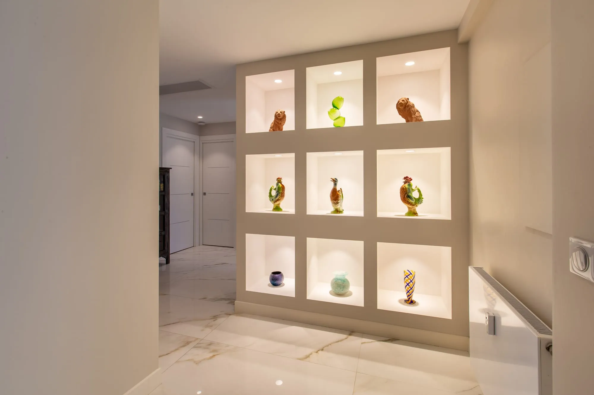 Mur de neuf niches éclairées dans l'entrée, sol clair veiné