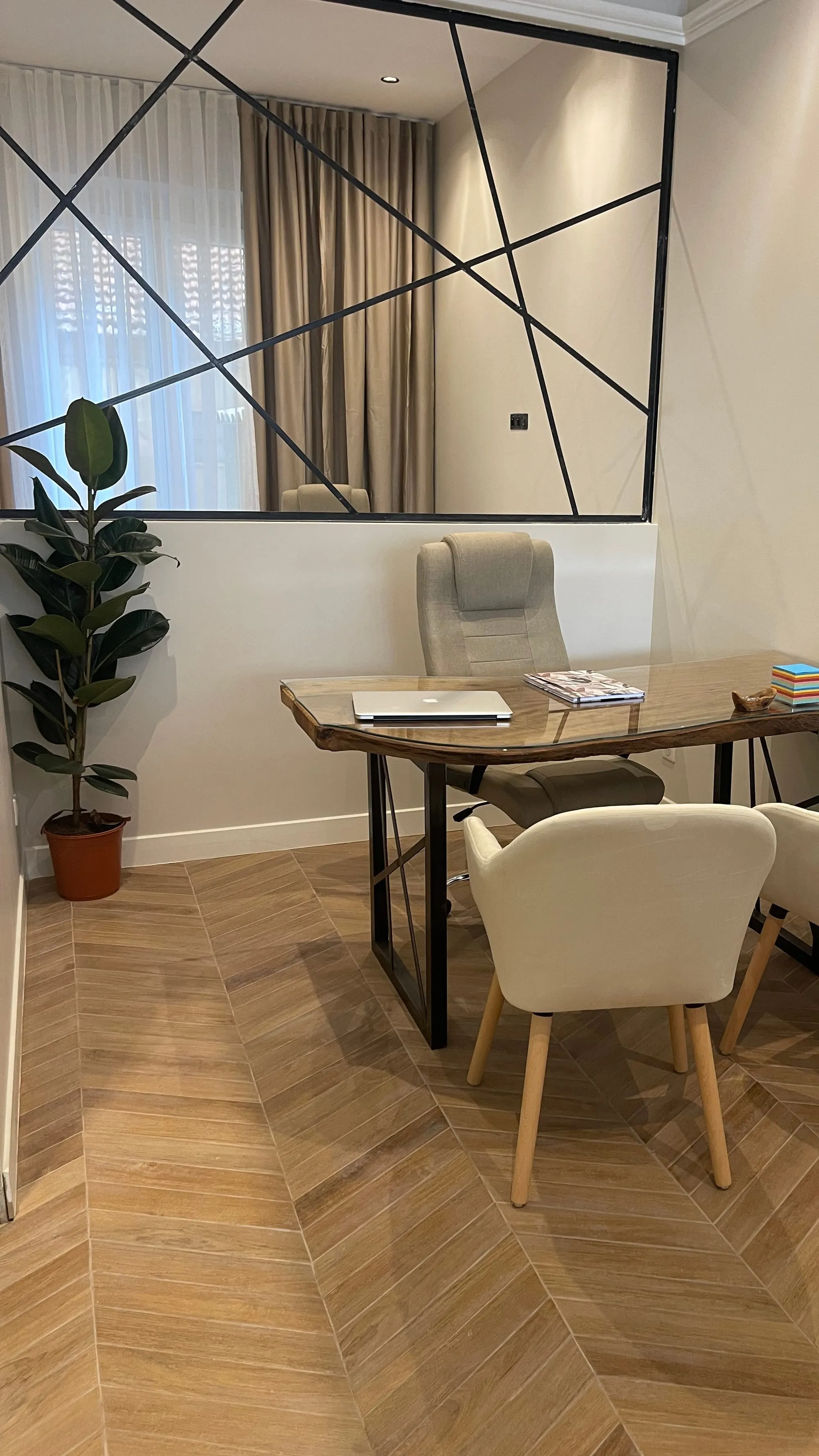 Bureau au plateau de bois brut, fauteuils clairs et sol en chevrons, devant un miroir mural quadrillé de noir