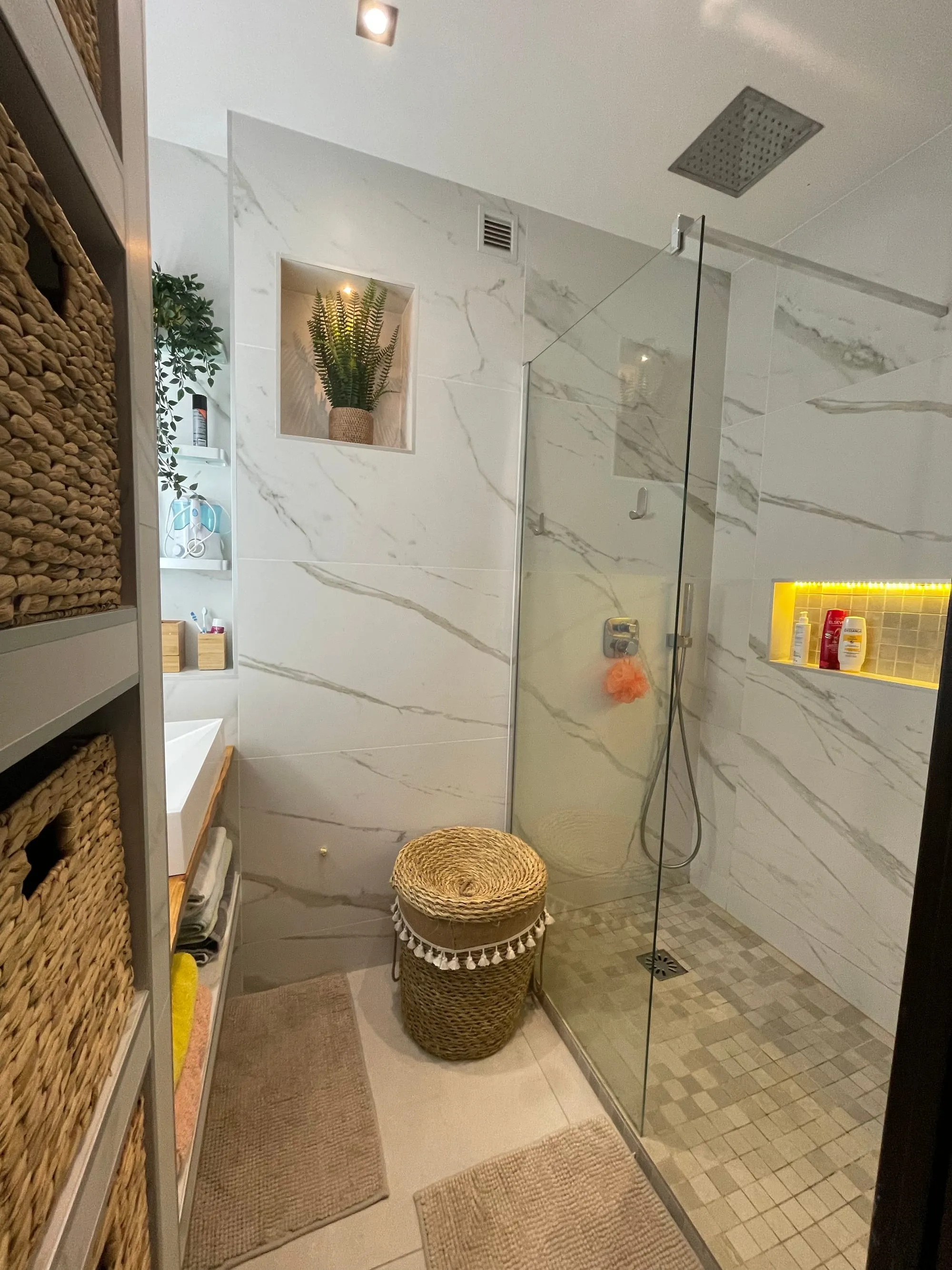 Salle d'eau aux murs veinés, douche de plain-pied derrière une paroi vitrée et niches éclairées