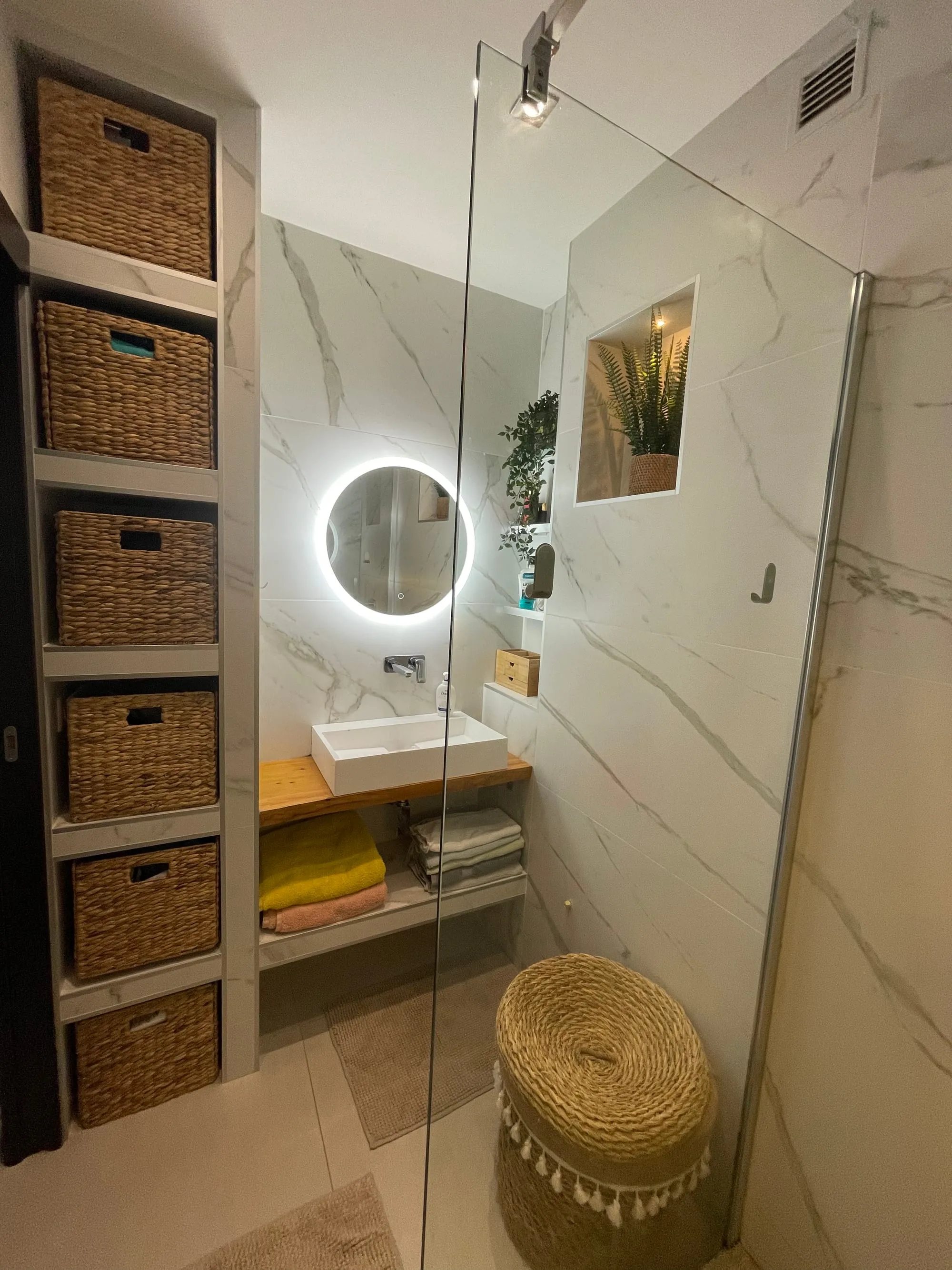 Salle d'eau avec étagères à paniers, vasque posée sur un plan en bois et miroir rond rétroéclairé