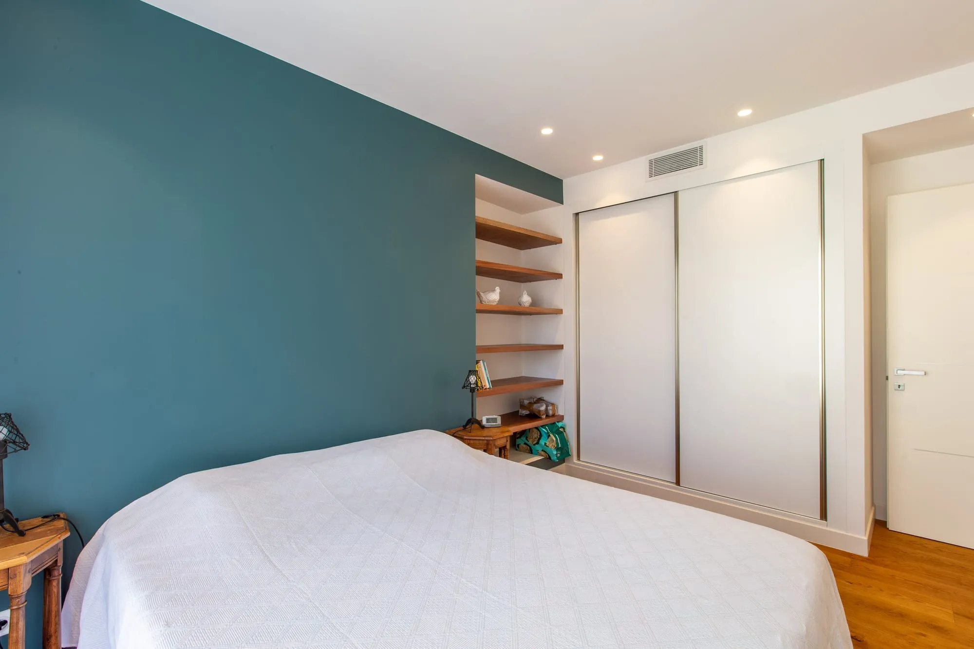 Chambre avec mur bleu canard, étagères en bois dans une niche et placard à portes coulissantes