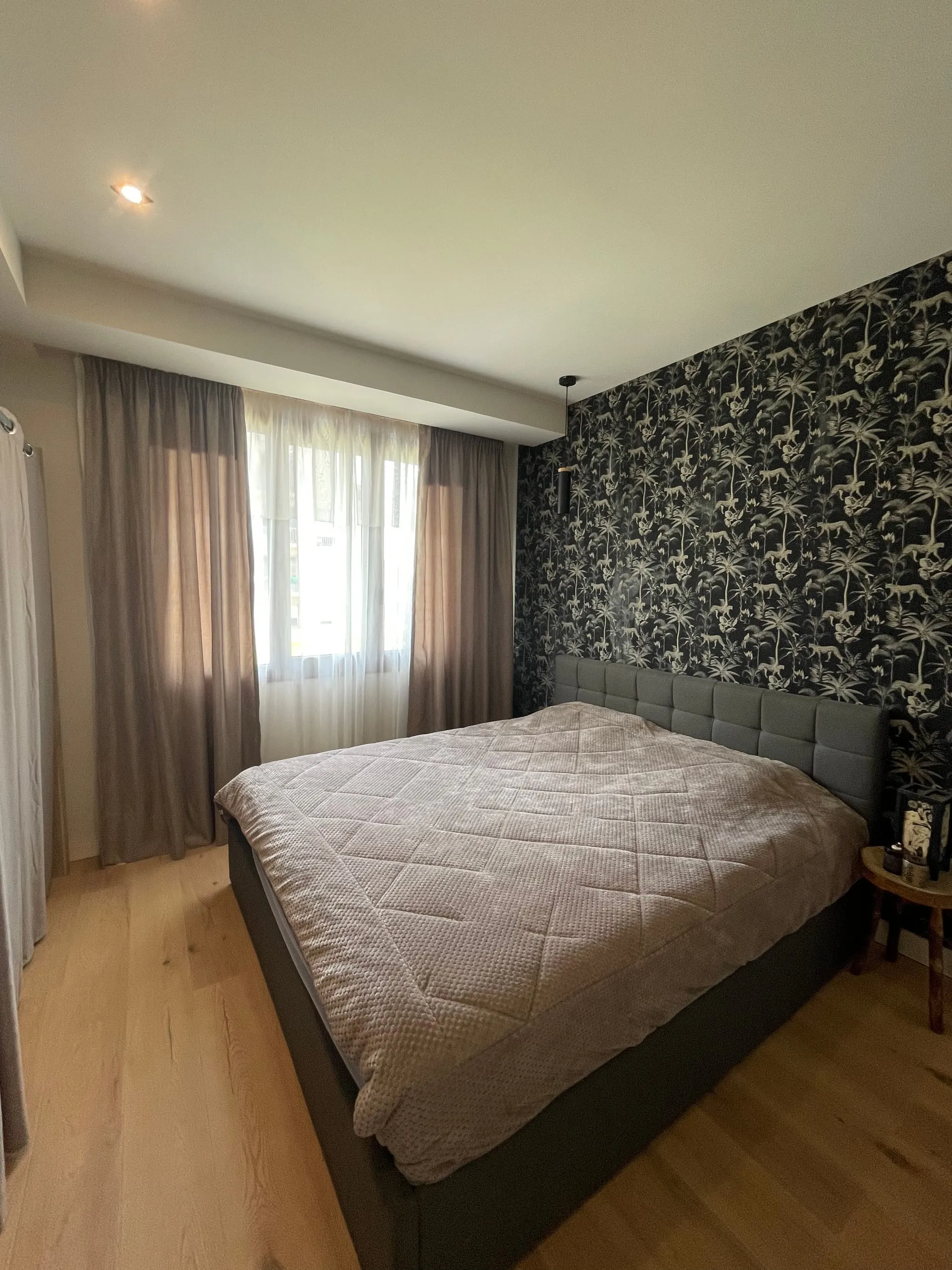 Chambre avec papier peint à motif de palmiers derrière le lit, parquet clair