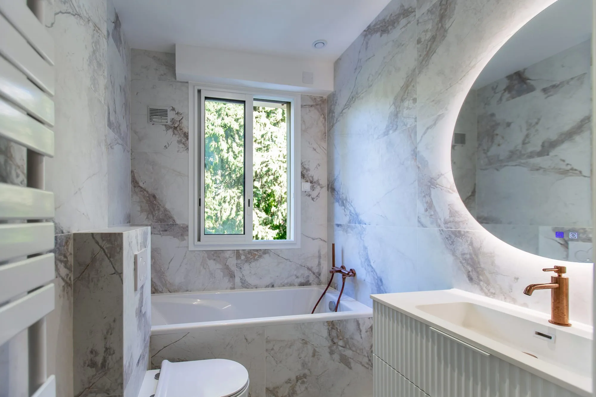 Salle de bains en marbre, baignoire sous fenêtre et miroir ovale rétroéclairé