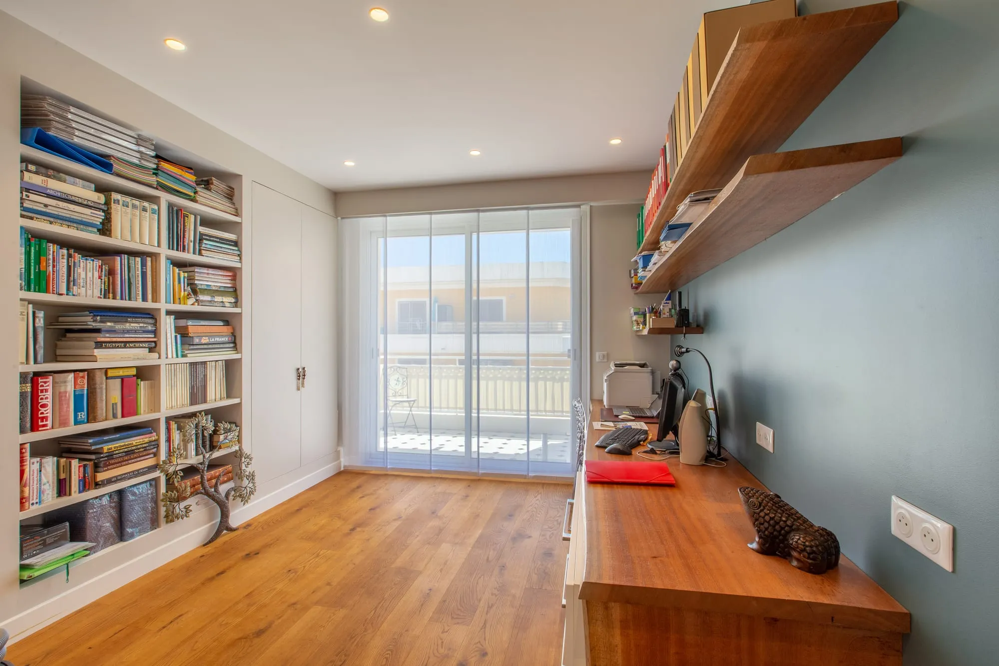 Bureau avec bibliothèque intégrée, étagères murales en bois et baie vitrée sur balcon