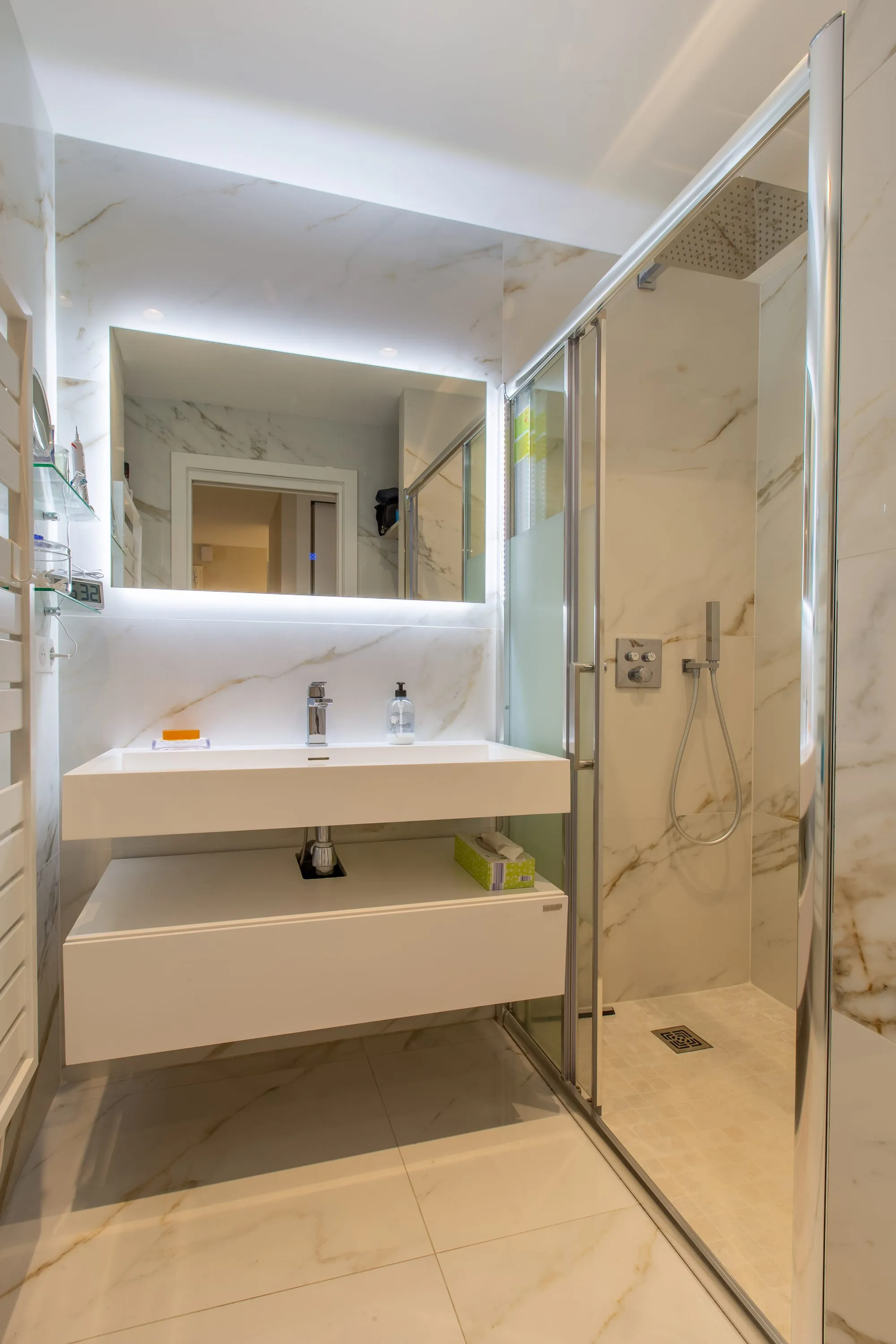 Salle d'eau avec vasque suspendue, miroir rétroéclairé et douche à paroi vitrée