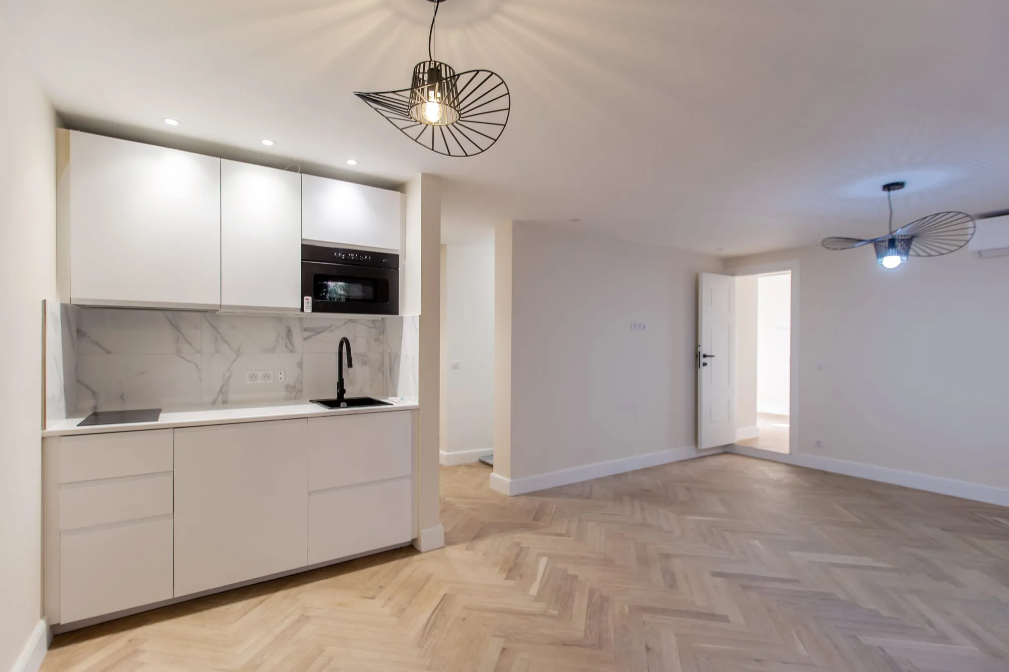 Cuisine blanche ouverte sur une pièce de vie, parquet point de Hongrie
